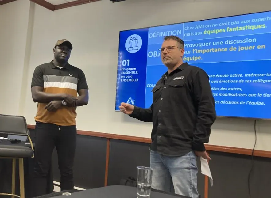 Deux animateurs devant un écran présentant un code culturel d’entreprise : « On gagne ensemble, on perd ensemble », lors d’une séance destinée aux gestionnaires.
