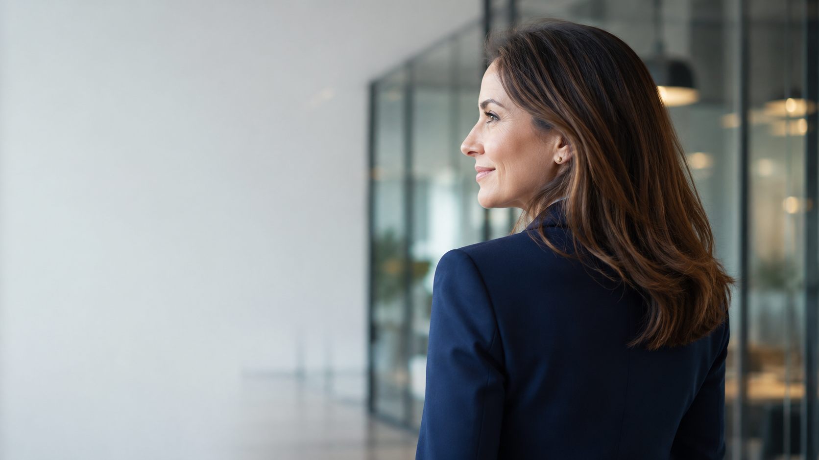 Femme d'affaires vue de dos et de profil, souriante, dans un couloir de bureau moderne