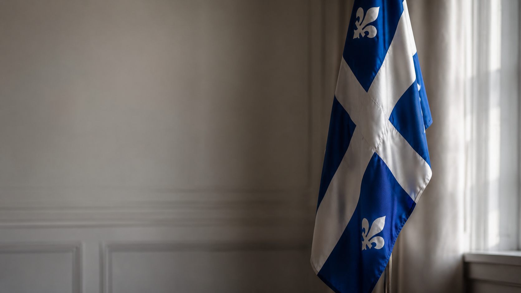 Drapeau du Québec suspendu dans une salle sobre, lumière naturelle filtrant par une fenêtre