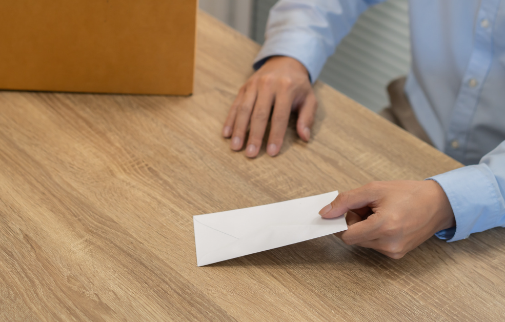 Une personne dépose une enveloppe sur un bureau, à côté d’une boîte de carton.