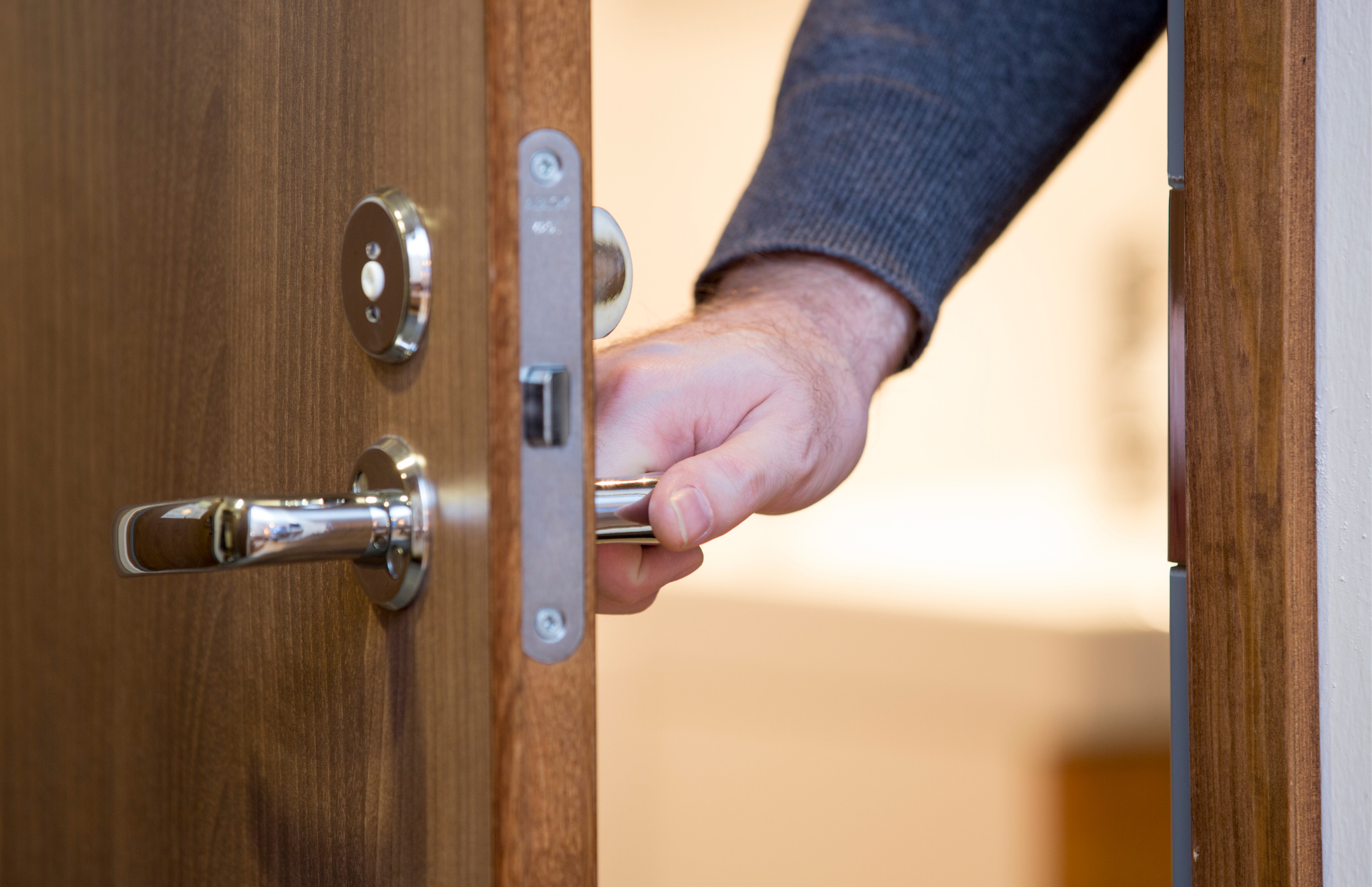Une main posée sur la poignée d’une porte entrouverte.