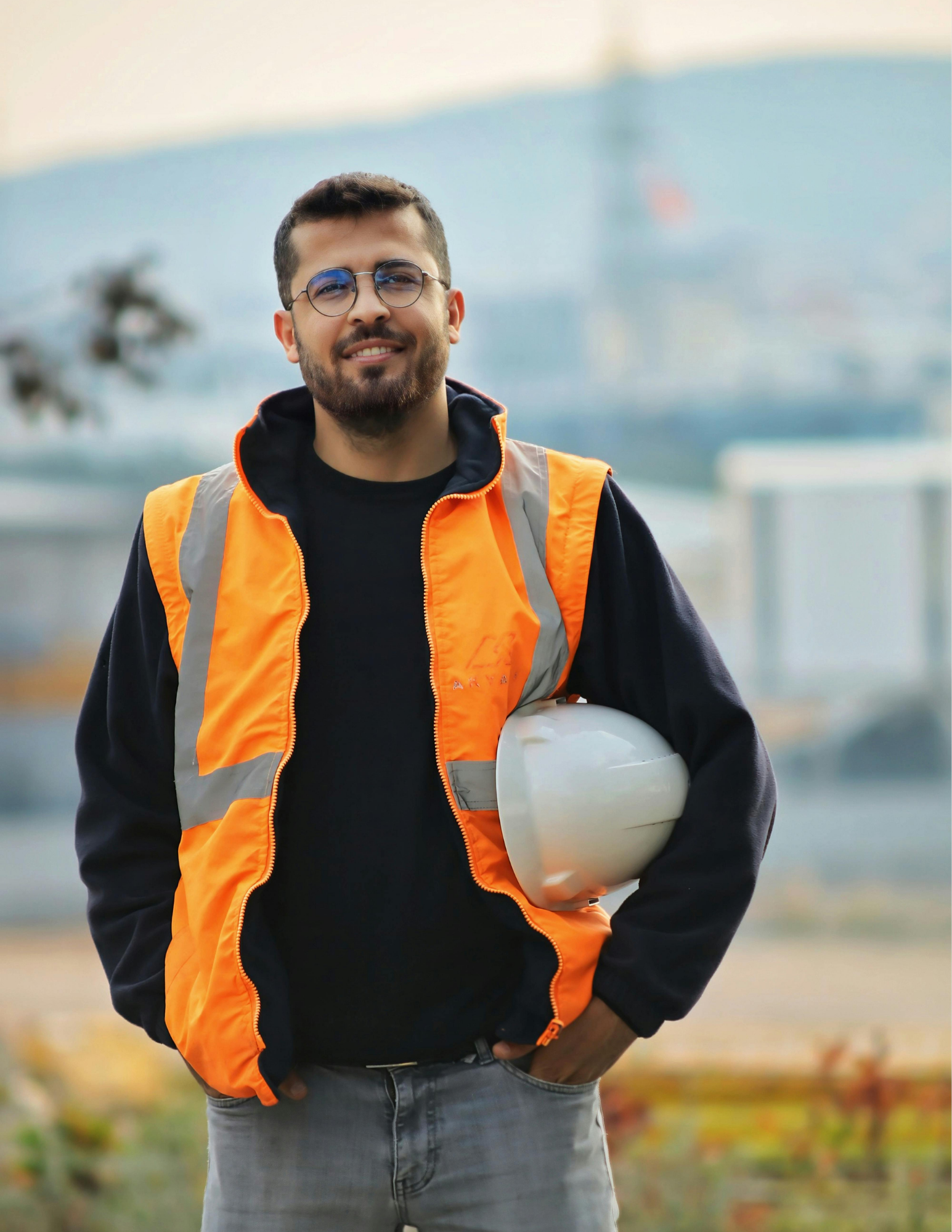 Un travailleur en veste haute visibilité tient son casque sous le bras, en milieu industriel.