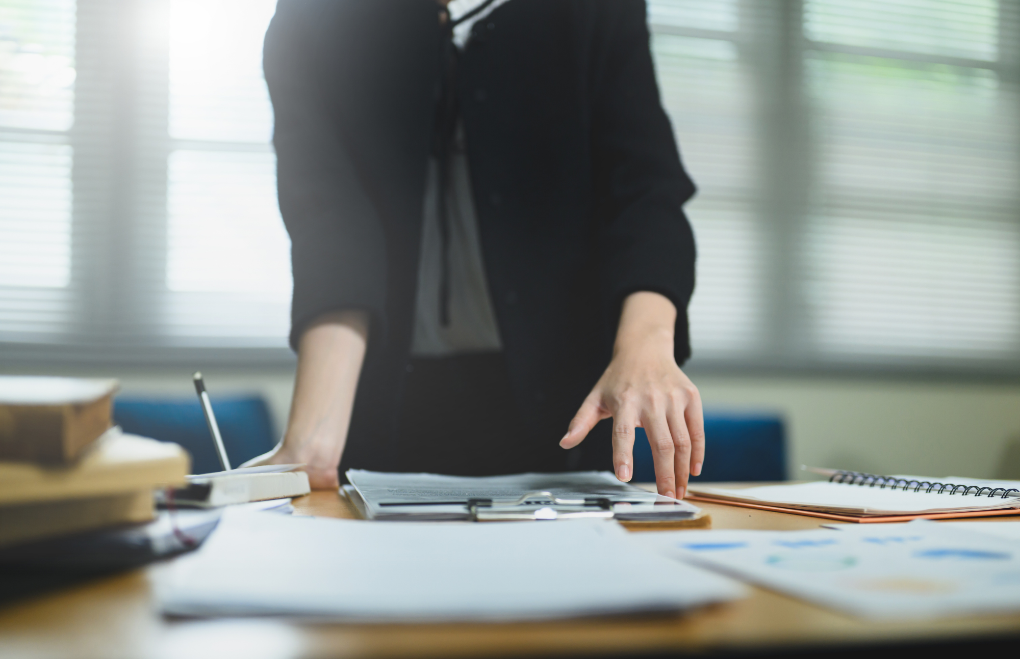 Une personne debout devant un bureau de travail où sont étalés documents, plans et cahiers de suivi.